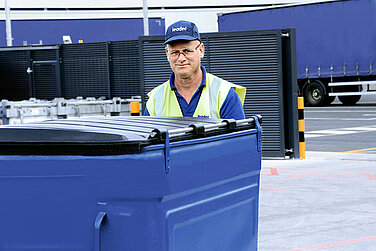 A Leadec employee pushing a dumpster at a waste yard.