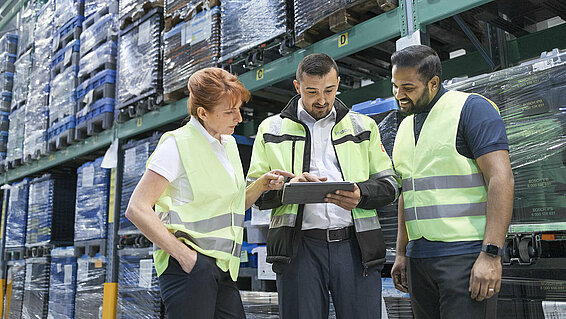 A group of Leadec employees looking at a tablet in a warehouse. 