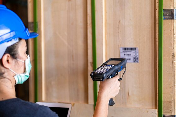 Worker with helmet scans a barcode on a wall with a handheld device.