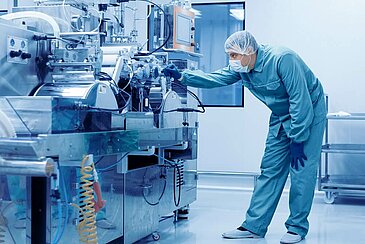 Man in protective clothing stands at a machine and inspects it.