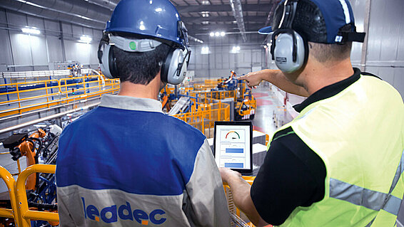 Two Leadec employees checking data with tablet and Leadec.os above shopfloor. 