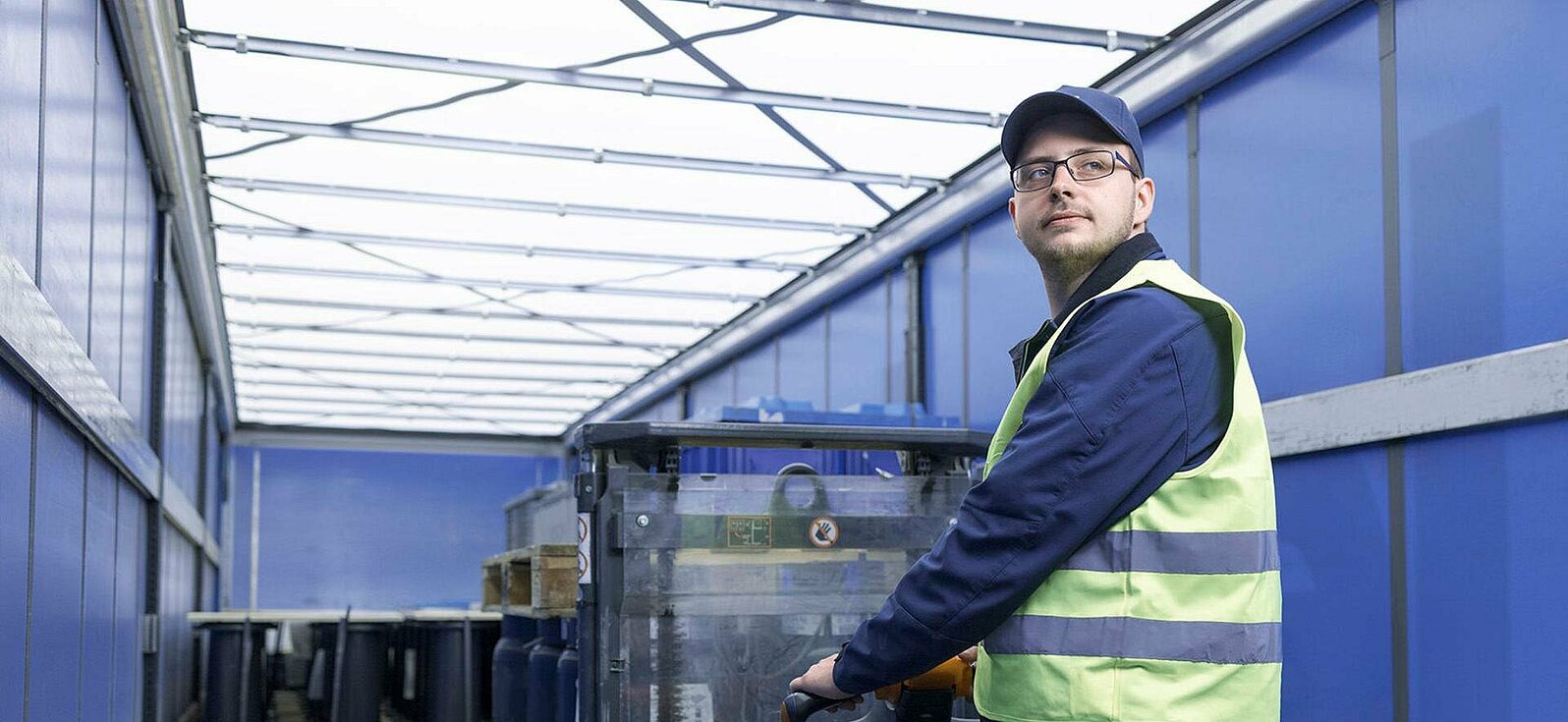A Leadec employee with safety vest loading a coil pallet from a truck with an electric pallet truck.